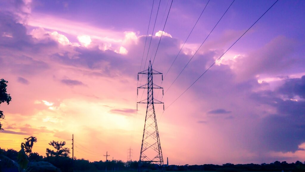 Silhueta de linhas de energia ao pôr do sol contra um céu vibrante roxo e laranja.
